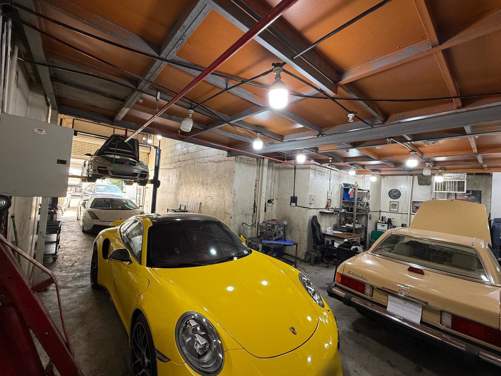 Inside the BOSS Garage workshop: a yellow Porsche 911 and a classic Mercedes-Benz SL in the bay, a Porsche on the lift behind