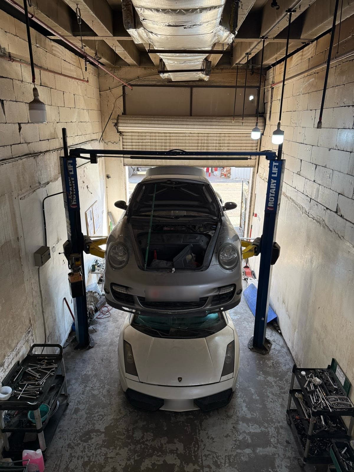 A Porsche 911 raised on a two-post lift above a white Lamborghini Gallardo